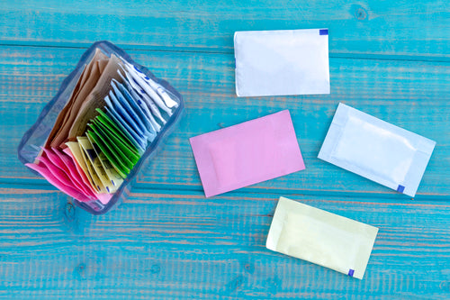 Packets of artificial sweeteners in glass container with individual packets sitting on bright blue wooden table