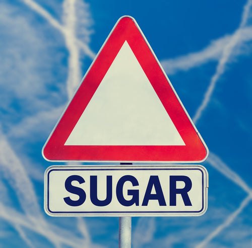 Sugar danger warning composed of white triangular traffic warning sign with the word - Sugar - below against a blue sky criss-crossed with contrails conceptual of the dangers of sugar in the diet.