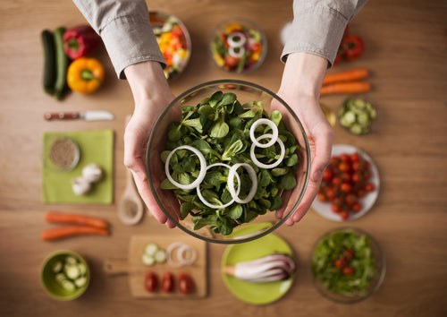 Hands holding an healthy fresh vegetarian salad in a bowl, fresh raw vegetables on background, top view